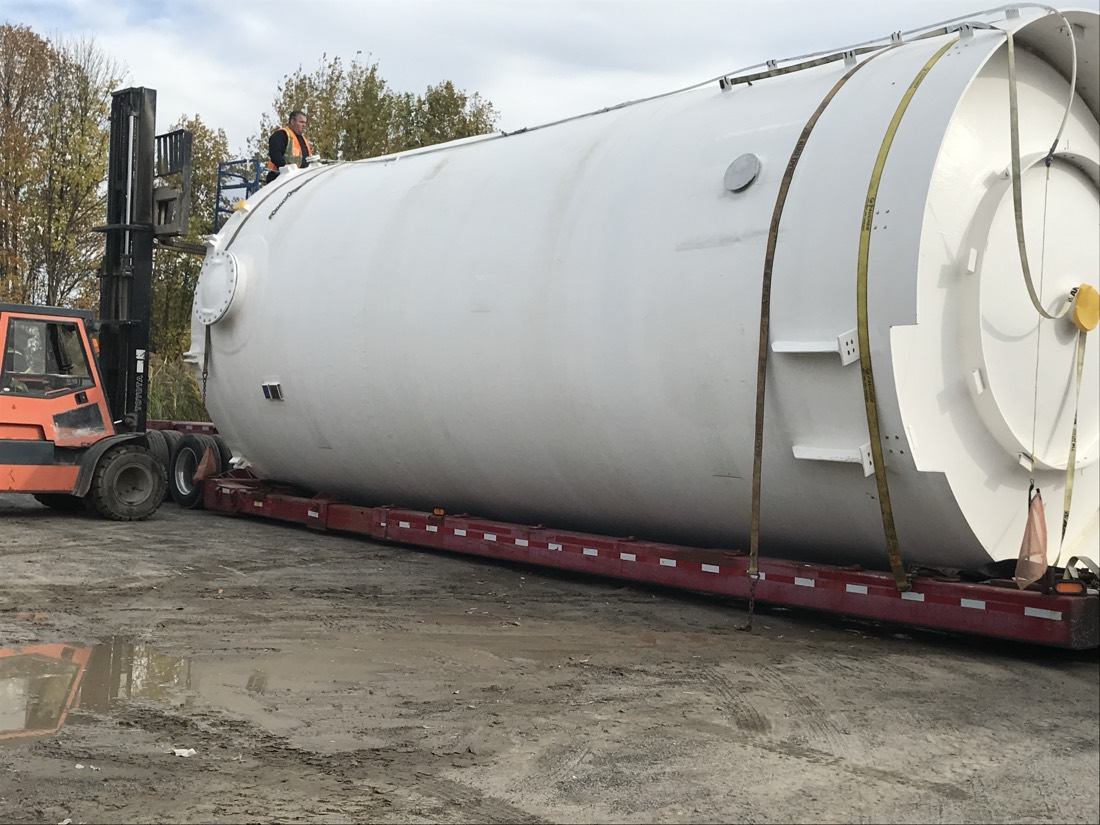 Large white industrial silo / tank on step-deck flatbed, orange forklift assisting