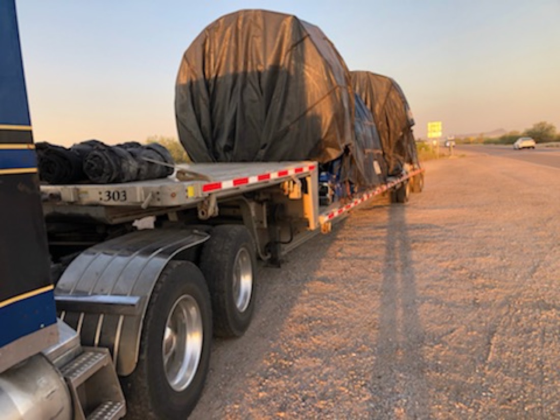 Same two tarp-wrapped loads on flatbed at desert roadside