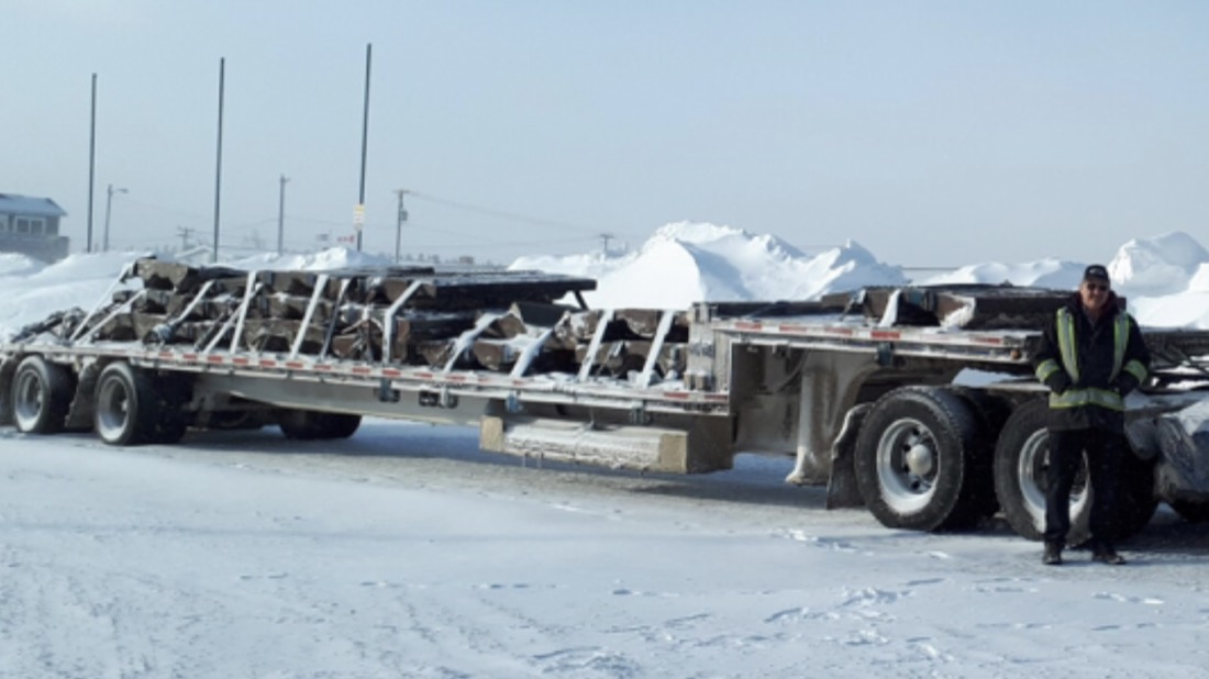 Worker by step-deck flatbed loaded with structural steel beams at arctic / northern site
