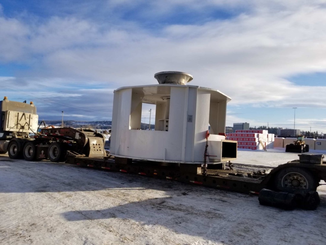 Large white industrial housing (crusher / mill feed bin enclosure) on lowboy in winter