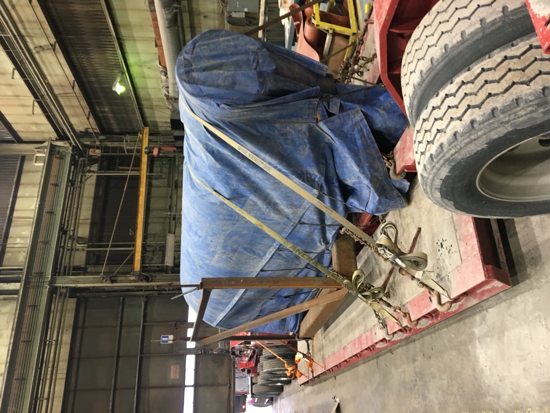 Same blue-tarp cargo on flatbed in shop — different angle with wheels visible