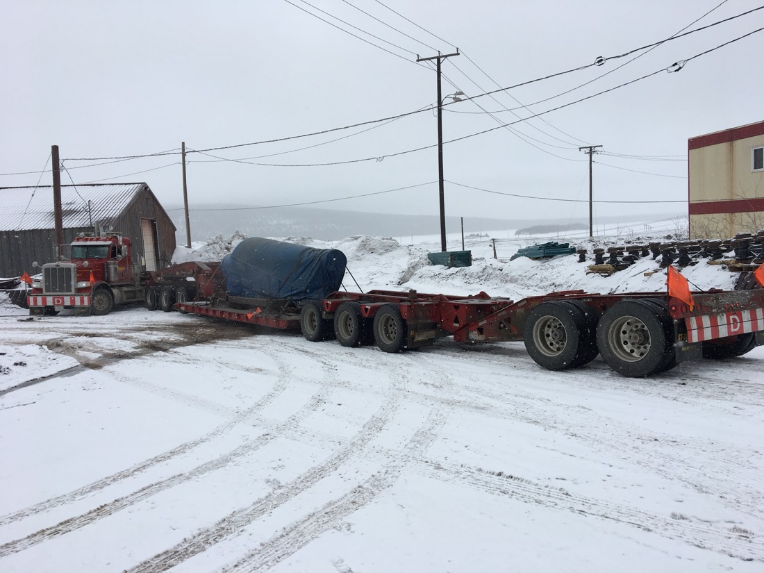 Red Peterbilt with blue-tarped cargo on multi-axle lowboy in winter mining yard