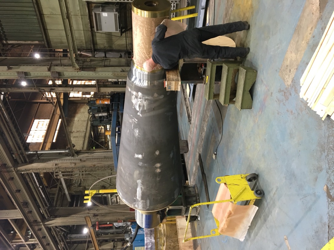 Worker preparing large industrial mill trunnion / drive shaft in fab shop