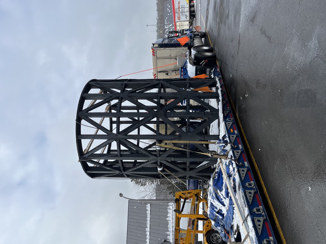 Same black tubular steel cage / cylindrical lattice frame on lowboy — different angle