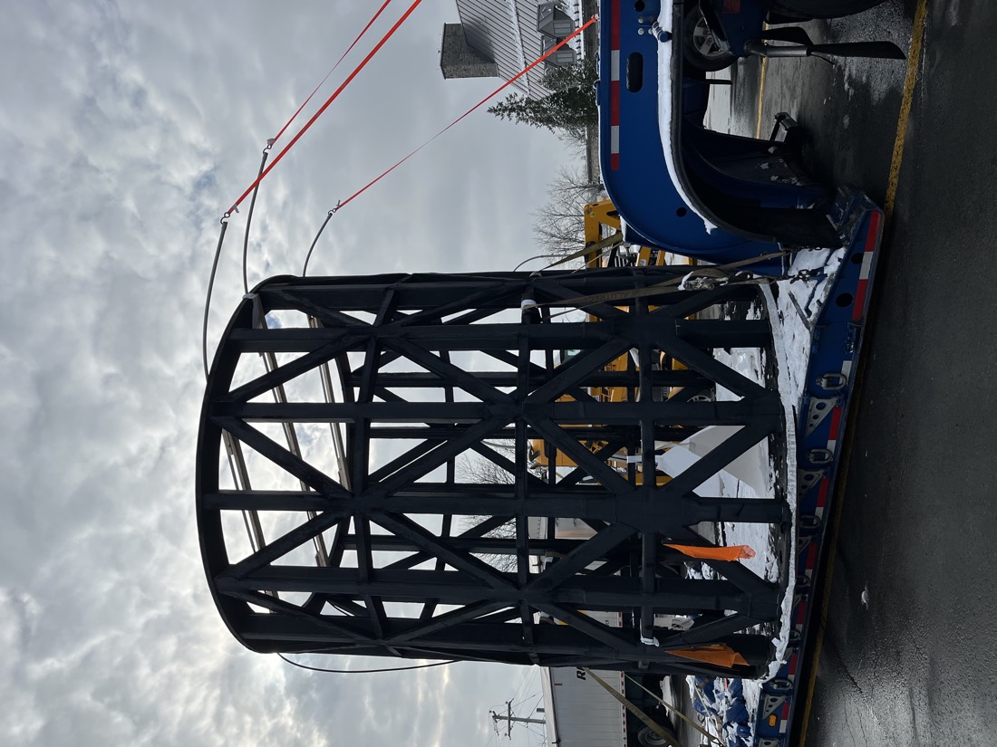 Same black tubular steel cage on lowboy with blue Kenworth — top-down rigging view