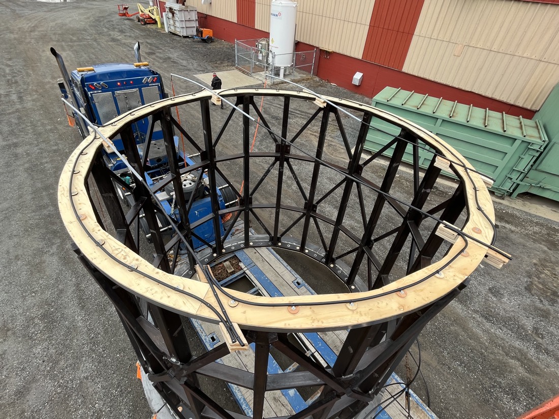 Top-down view of cylindrical structural cage being unloaded from blue Kenworth