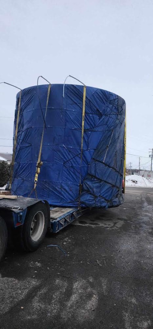 Large blue-tarp-wrapped cylindrical industrial tank / vessel on lowboy trailer in winter