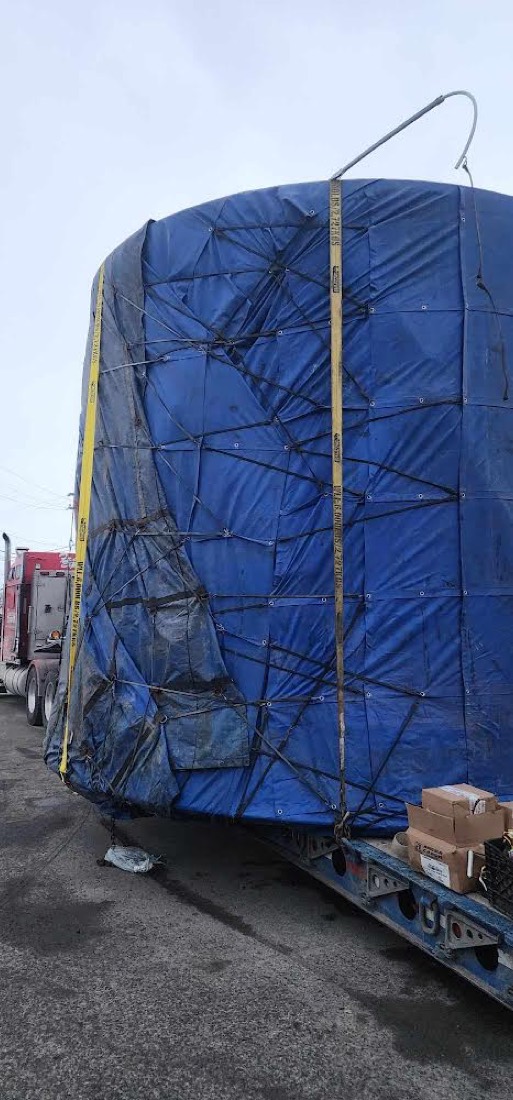 Same large blue-tarp-wrapped industrial tank on lowboy — closer side view