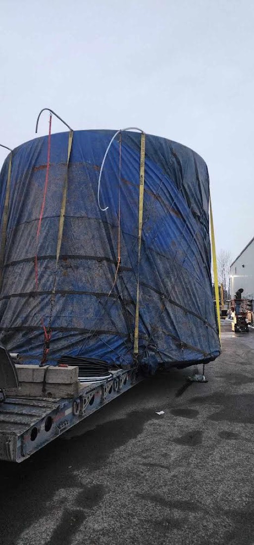 Same blue-tarp-wrapped tank on lowboy — rear view, evening light