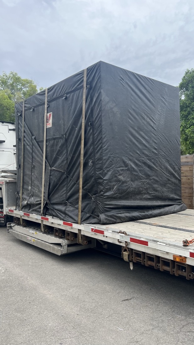 Black-tarp covered shipping crate strapped on step-deck flatbed