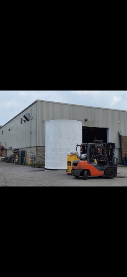 Forklift loading large white wrapped vessel at warehouse loading dock