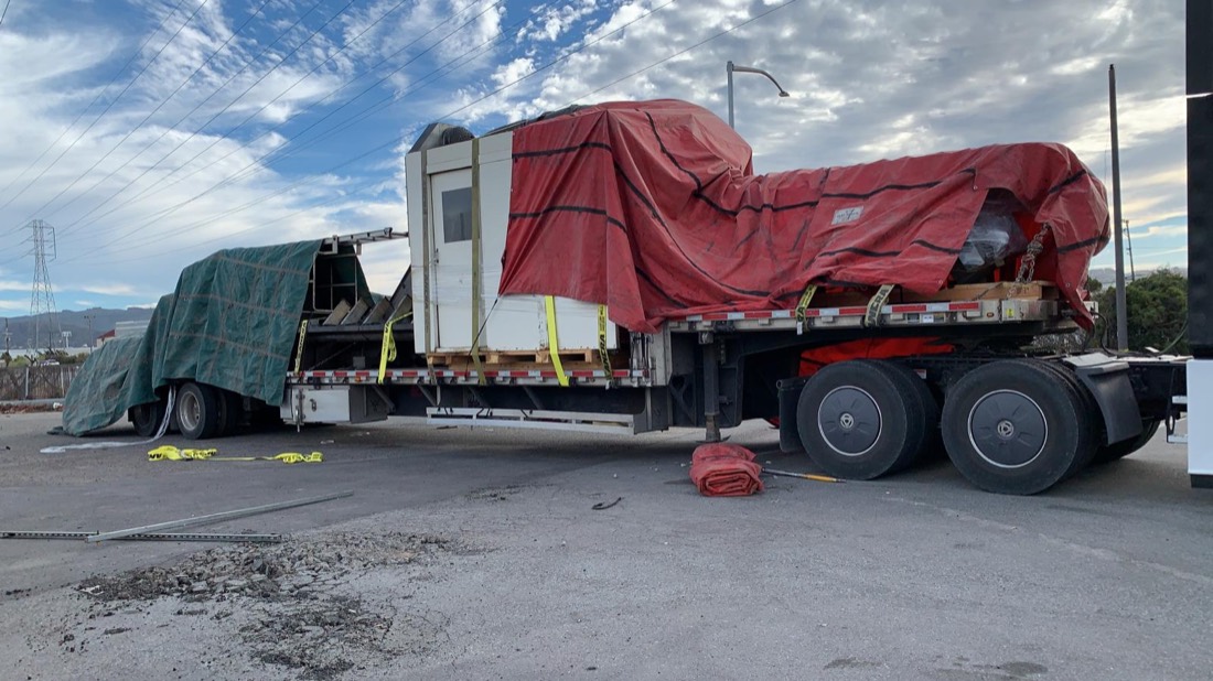 Mori Seiki CNC machine + cabinet under red and green tarps on step-deck flatbed