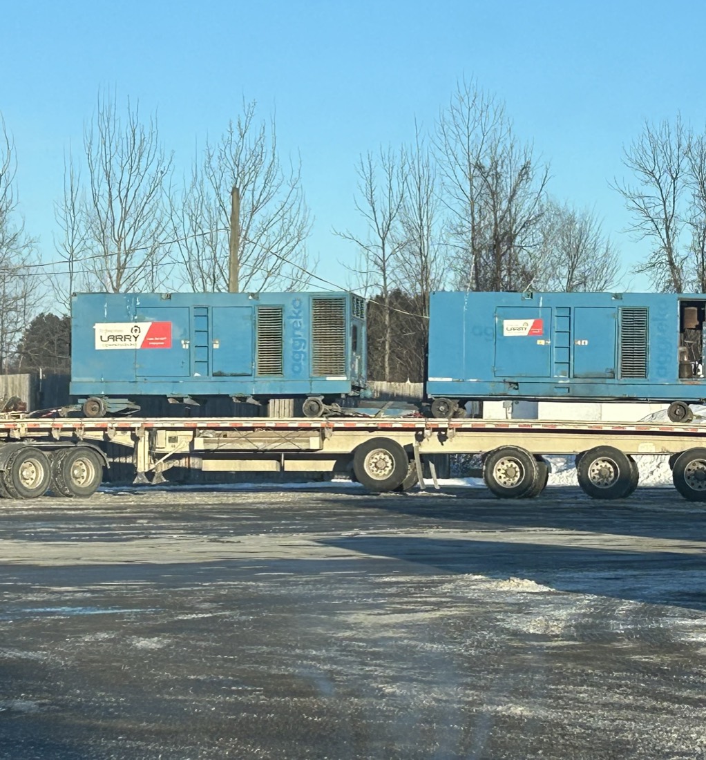 Two blue Larry Transport diesel gensets loaded on multi-axle flatbed