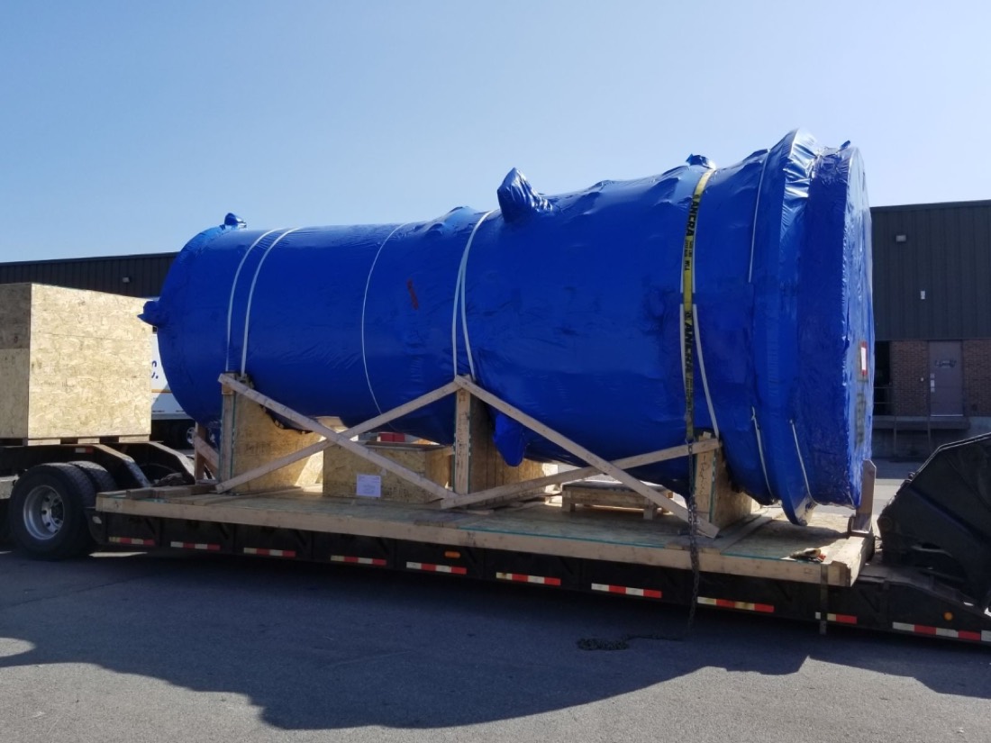 Blue-tarped industrial cyclone separator / process vessel on wood skid on step-deck flatbed
