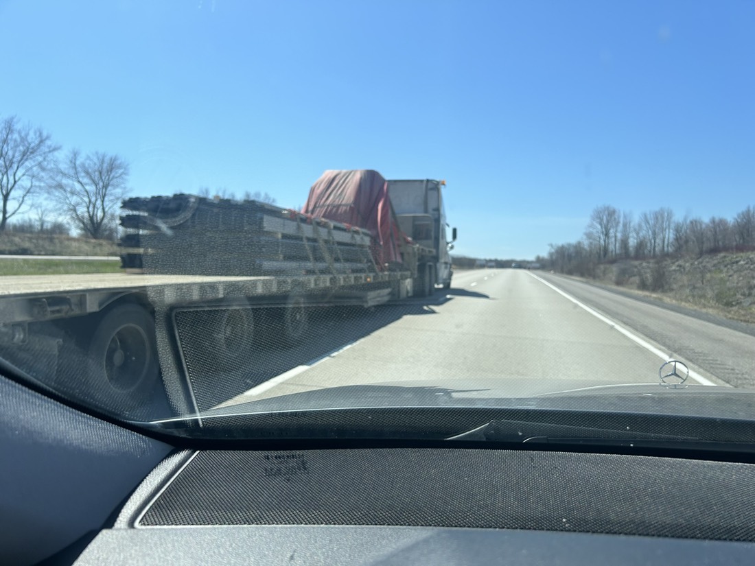 Mercedes dashboard view of flatbed with stacked steel pipe / tubing on highway