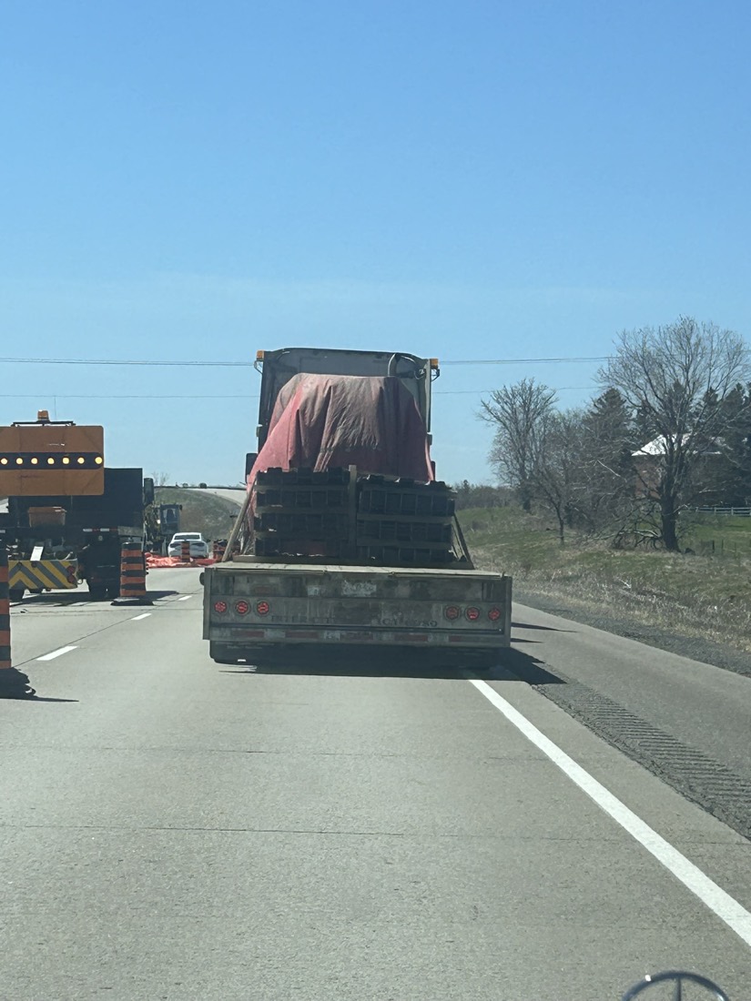 Rear view of flatbed with red-tarped pallets on highway construction zone