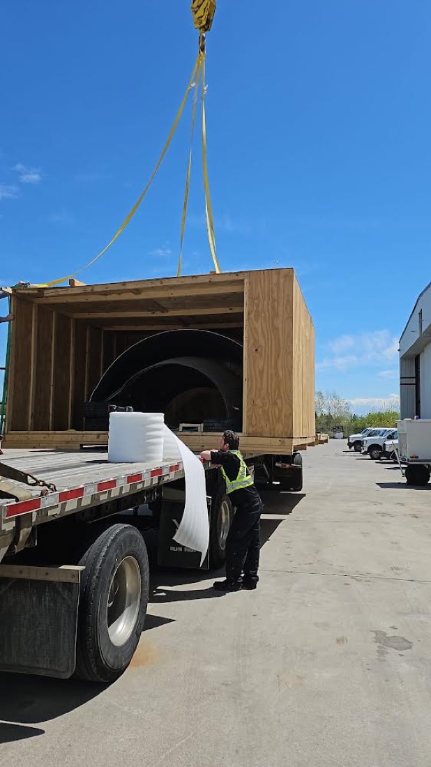 Aircraft fuselage section inside wooden shipping crate being loaded on flatbed