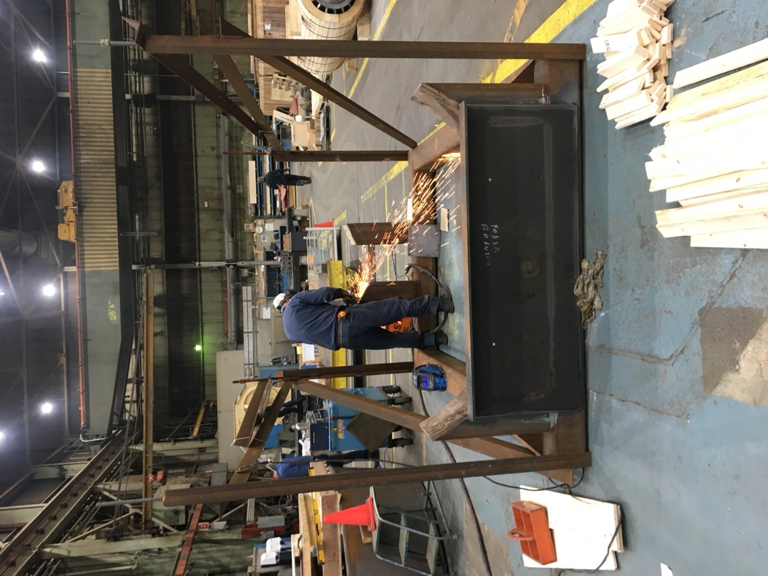 Worker grinding on large steel girder in fabrication shop