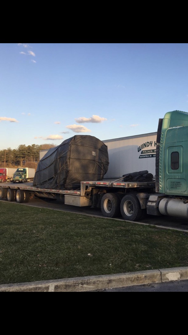 Green Kenworth with tarp-wrapped cargo on step-deck flatbed at rest stop