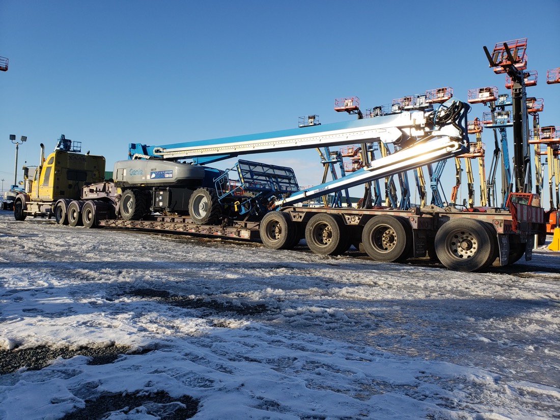 Genie / Skyjack telescopic boom lift on lowboy at equipment rental yard (winter)