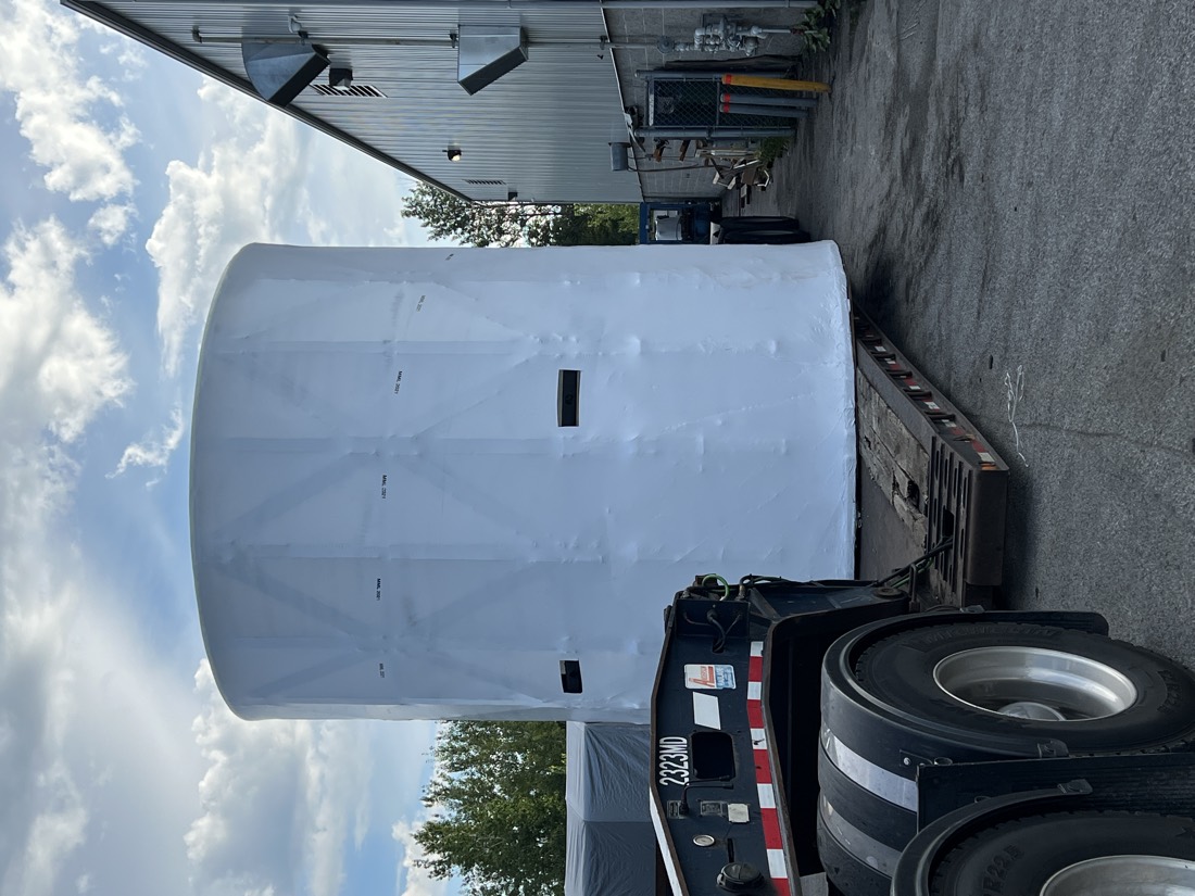 Large white shrink-wrapped cylindrical vessel / tank on lowboy at industrial yard