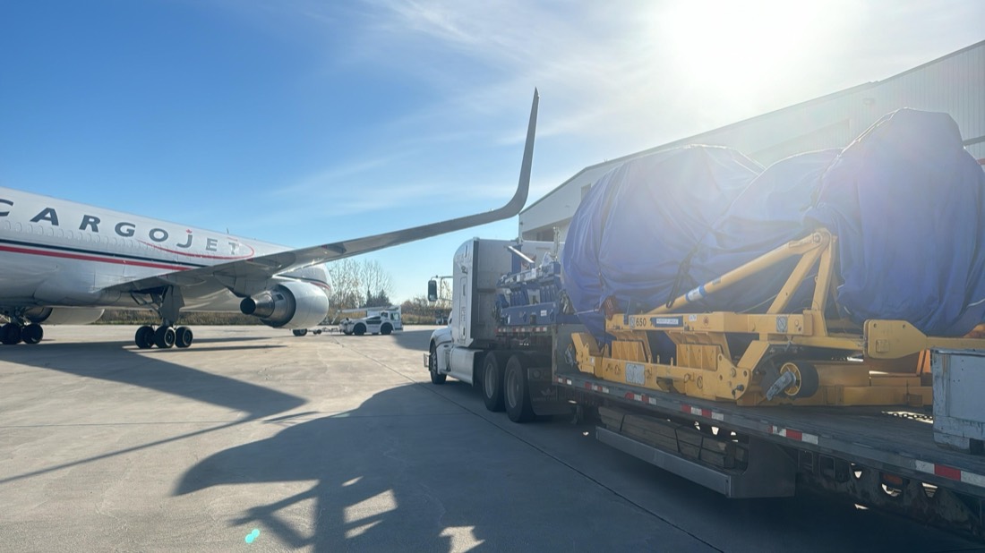 Jet engine on yellow stand under tarp on flatbed alongside parked Cargojet 767