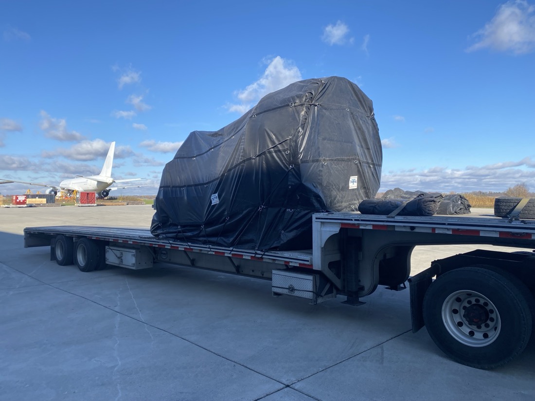 Black-tarped jet engine on stand + aircraft tires on step-deck at airport (Boeing behind, dup of IMG_3539)