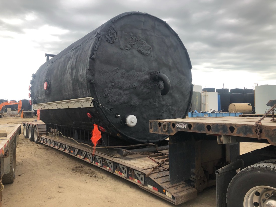 Large black-coated insulated tank / vessel on Deen lowboy at oilfield yard