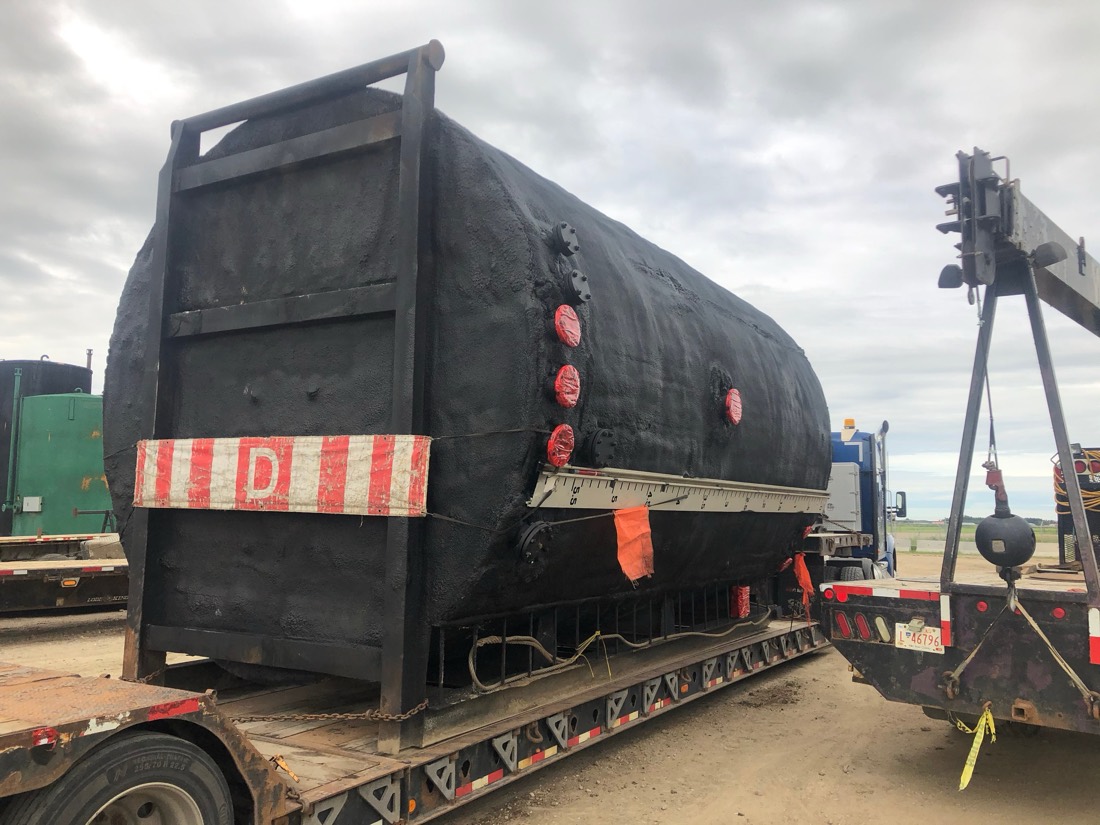 Same black-coated insulated tank on lowboy — rear view with OVERSIZE LOAD banner