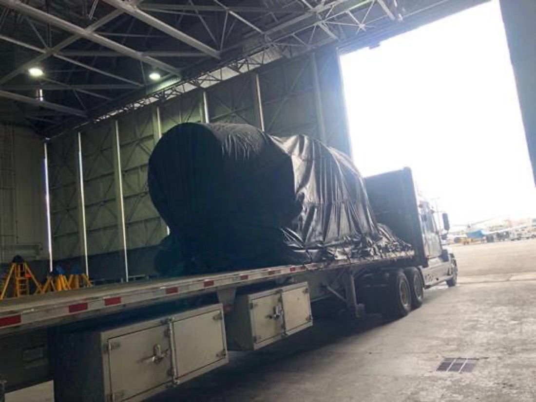 Black-tarped jet engine on stand on flatbed inside hangar