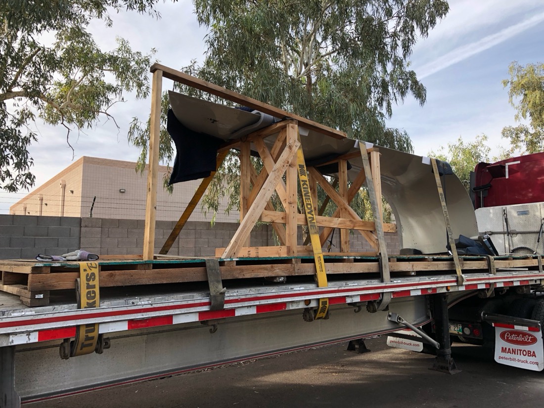 Fiberglass boat hull on wood cribbing on flatbed with Manitoba Peterbilt