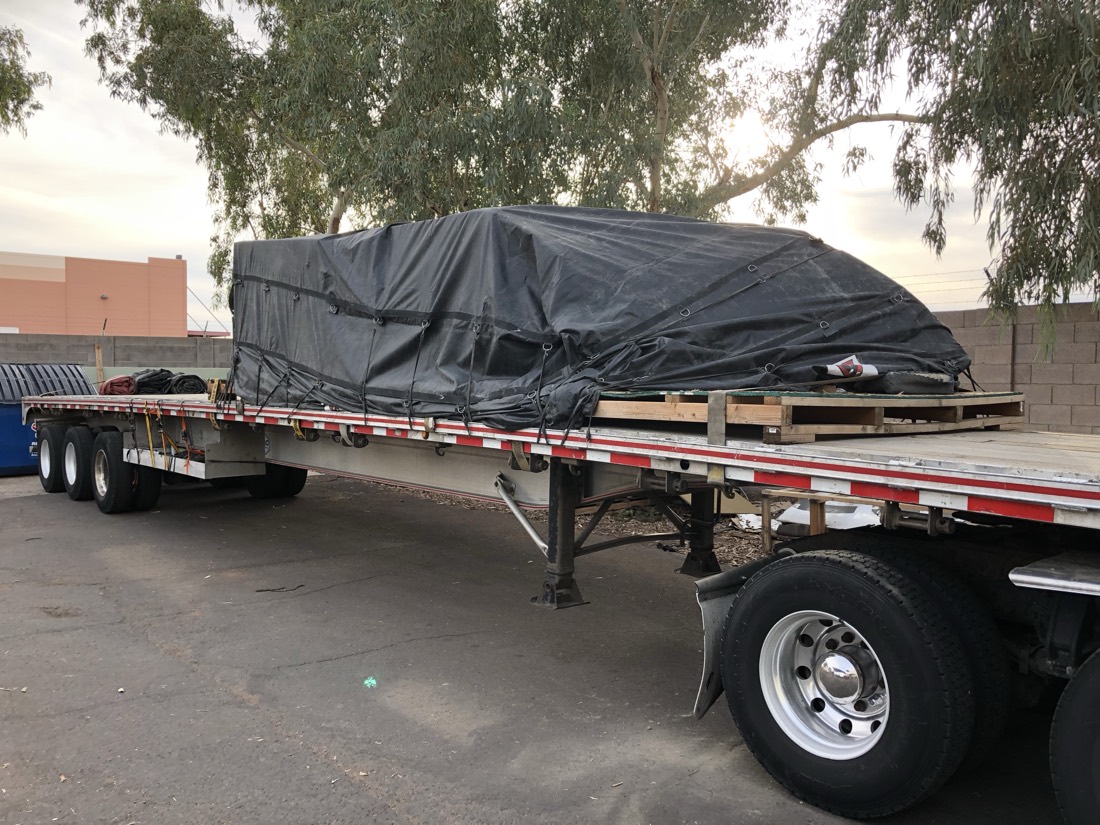 Same boat hull cargo now black-tarp-covered on flatbed
