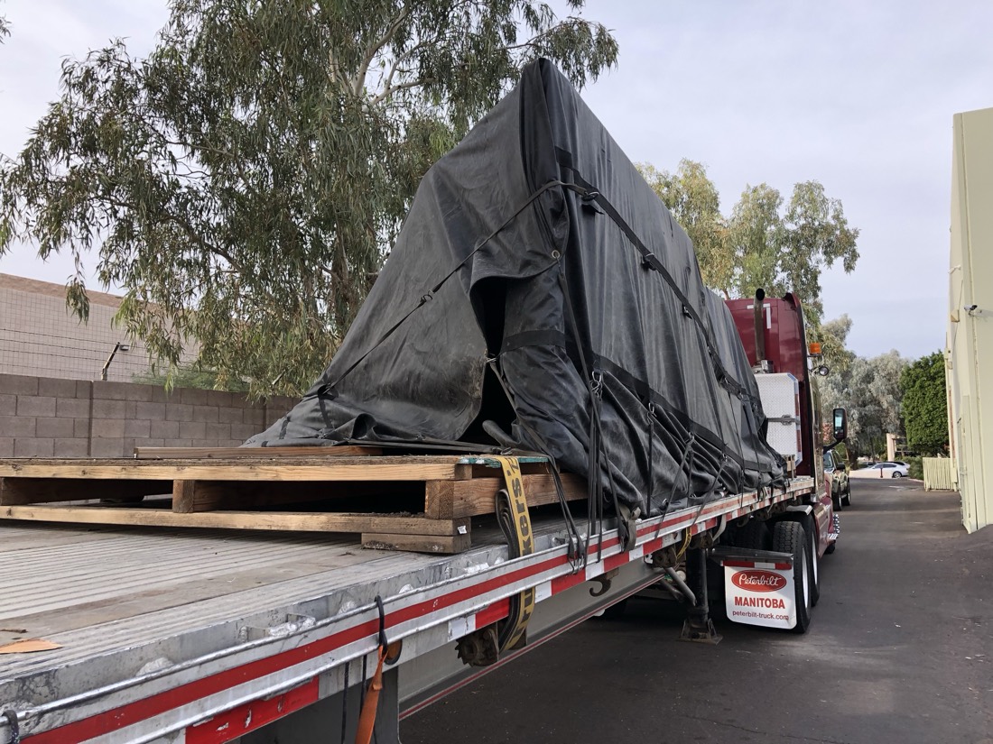 Same tarp-covered boat hull on Manitoba Peterbilt flatbed — different angle