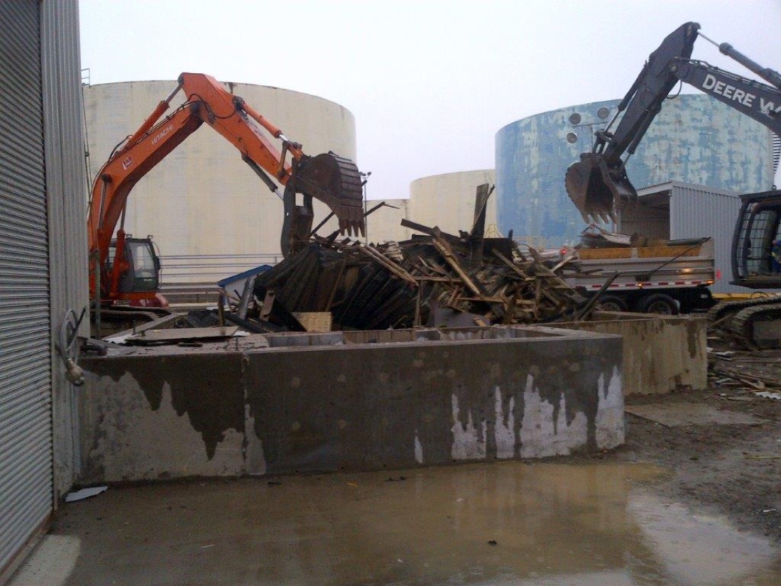 Hitachi & John Deere excavators demolishing steel structure at refinery tank farm