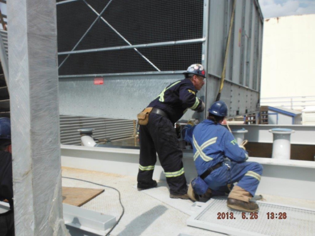 Workers installing cooling tower module bolts at refinery rooftop