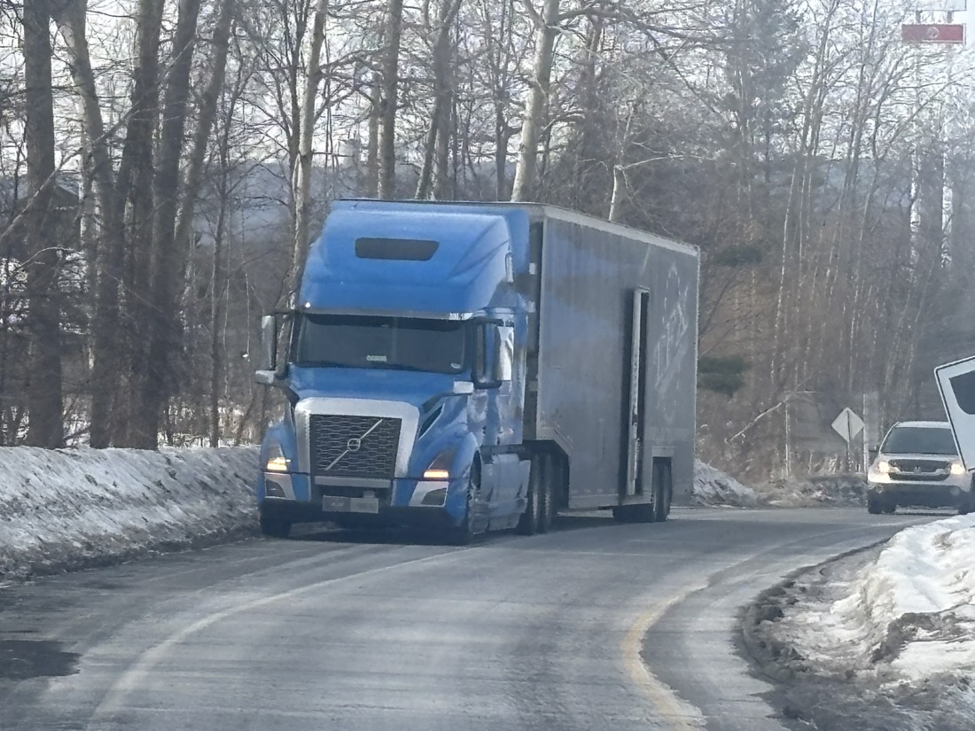 Blue Volvo tractor pulling enclosed trailer through tight winter curve