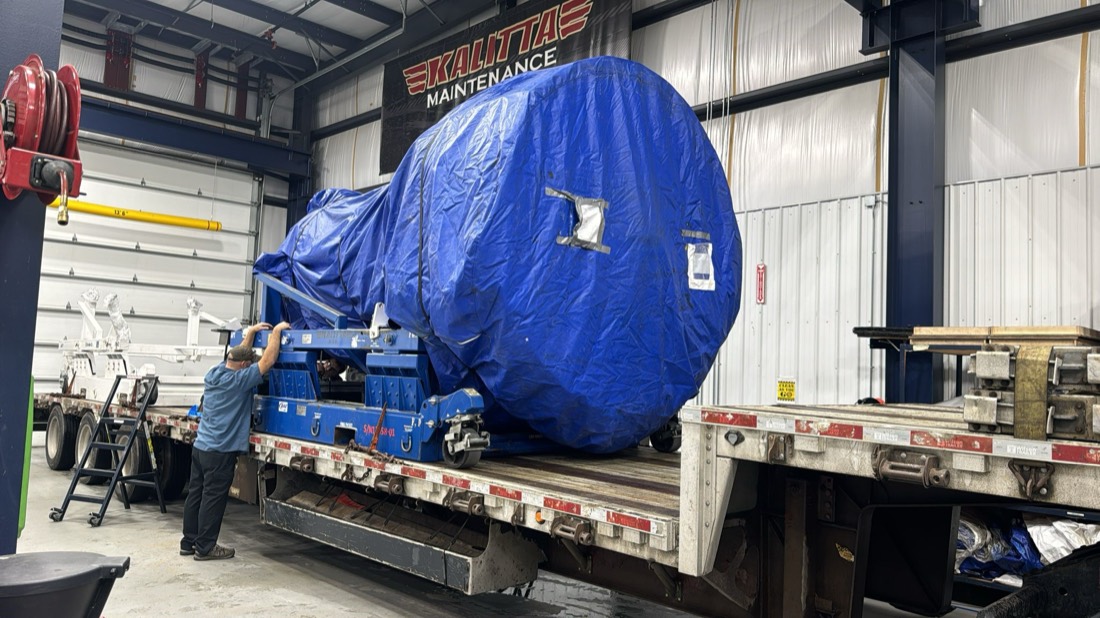 Blue-shrouded jet engine on transport stand inside Kalitta Maintenance hangar