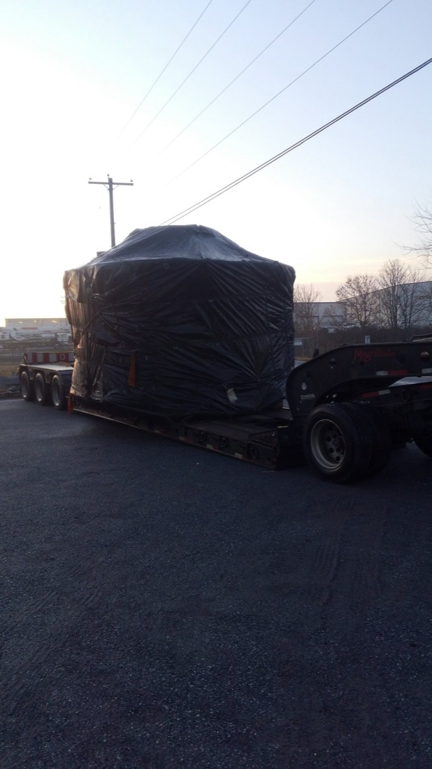 Boxed machinery wrapped in black shrink and tarp on Magnitude lowboy at dusk