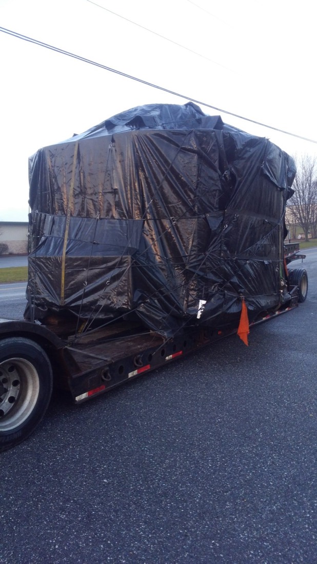Side view of same shrink-wrapped industrial crate on stepdeck, roadside