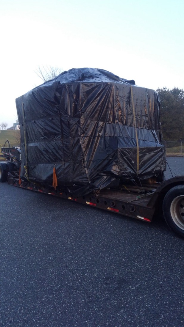 Rear-quarter angle of shrink-wrapped machinery load on lowboy at sunset