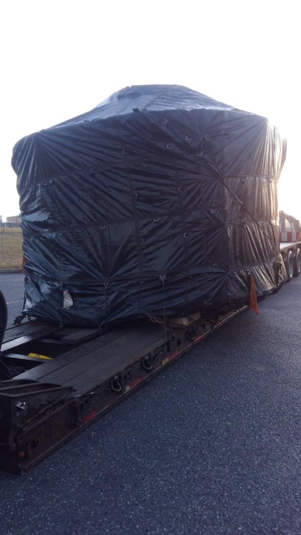 Profile of black-wrapped equipment load tied down to drop-deck trailer