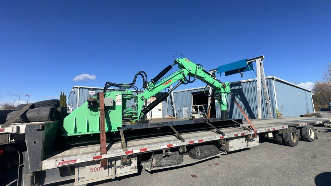 Green Trimax mower/road-edger attachment chained to stepdeck trailer
