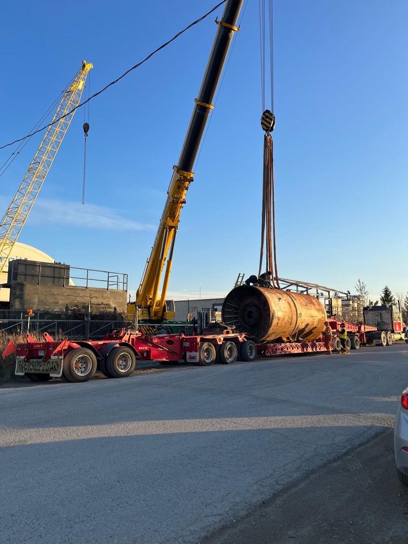 Tandem-crane lift of TBM cylinder onto red Aspen multi-axle lowboy in yard
