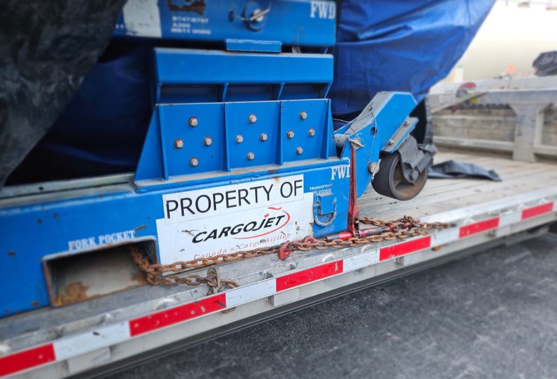 Cargojet-branded blue jet engine stand bolted to flatdeck, chained for transport
