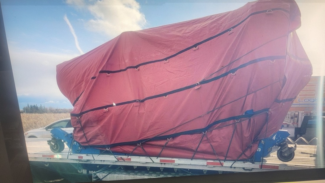 Red tarp-shrouded oversize load with Brampton Straps netting — front-three-quarter view from cab