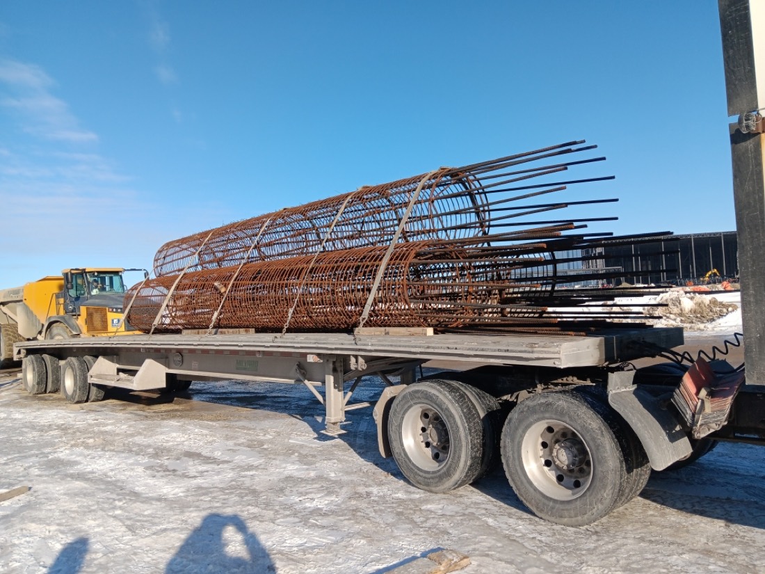 Same bundled rebar pile cages on flatdeck with articulated dump truck behind