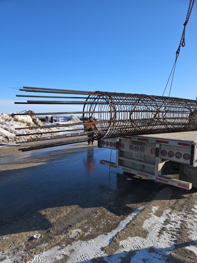 Rebar cage being lifted off rear of flatdeck — workers in hi-vis directing the lift