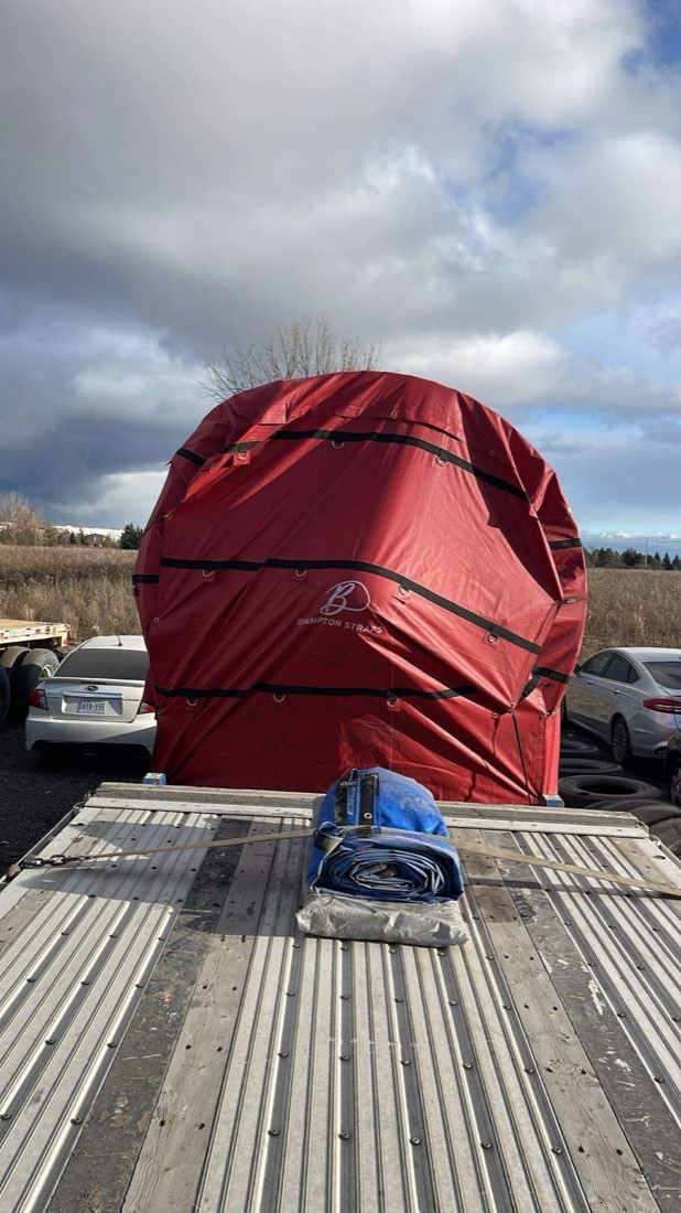 Bell-mouth tarped load (Brampton Straps net) viewed from behind on stepdeck — rural roadside