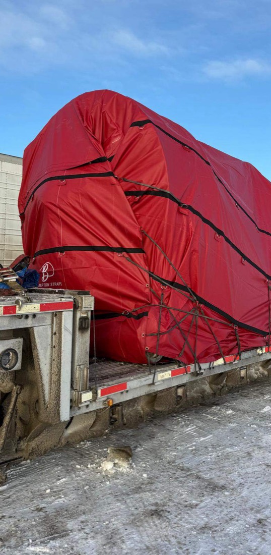 Side view of same red tarp-covered bell load on flatdeck at winter dusk