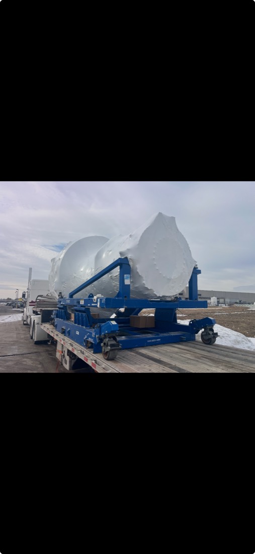 White-wrapped curved component cradled on blue Schreuder-style trailer beam at winter site
